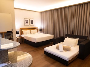 Ein Hotelzimmer mit zwei Betten, einem Schreibtisch, einem Stuhl, einer Lampe und einem großen Fenster mit Vorhängen.