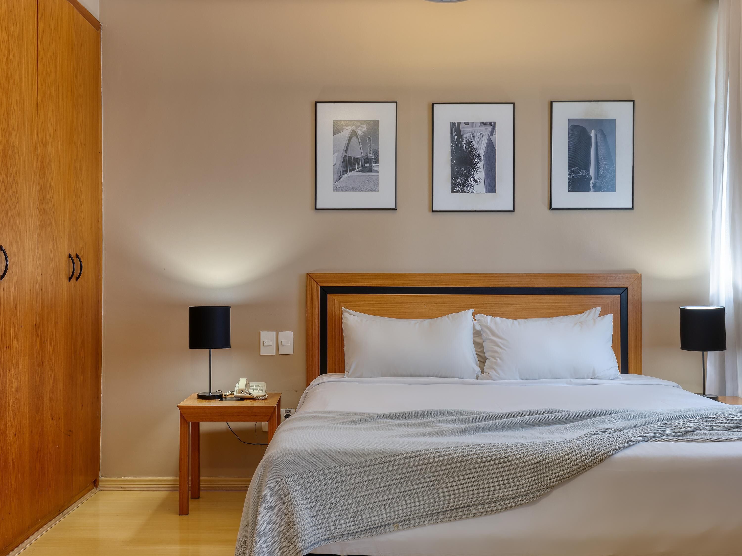 Habitació d'hotel amb un llit, abacines, una taula de nit i tres quadres penjats a la paret.
