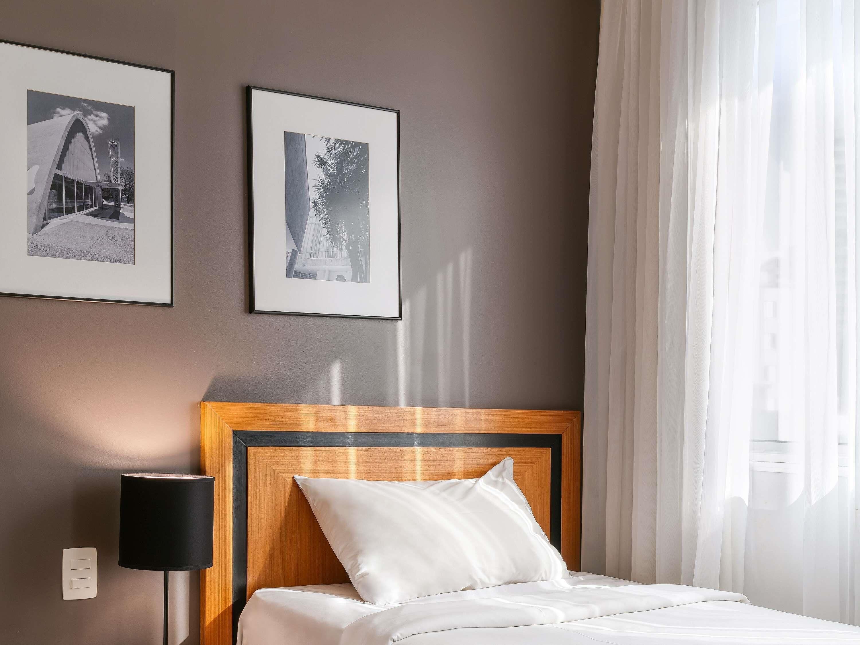Hotellihuone, jossa on sänky, yöpöytä, lamppu ja kaksi kehystettyä kuvaa seinällä.