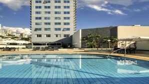 Un hotel moderno con piscina, un edificio alto al fondo y cielo despejado.