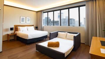Habitación de hotel con dos camas, un sofá, un escritorio y vistas a la ciudad.