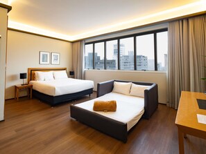 Une chambre d’hôtel avec deux lits, un canapé, un bureau et une vue sur la ville.