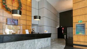 Zona de recepción de un hotel con mostrador de mármol, una pared de madera con un adorno navideño y un cartel con el nombre del hotel.