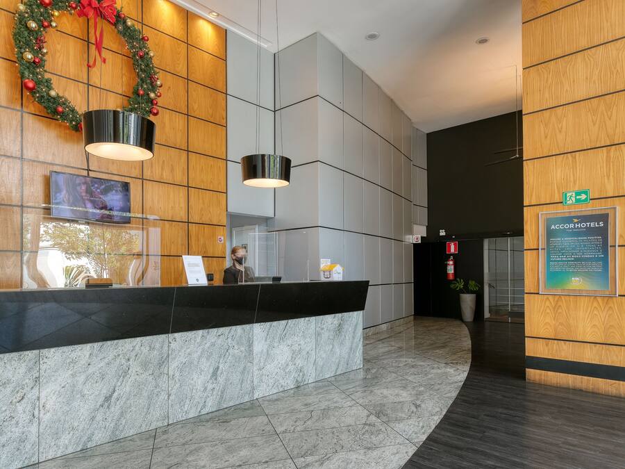 A hotel reception area with a marble counter, a wooden wall with a Christmas wreath, and a sign indicating the hotel name.