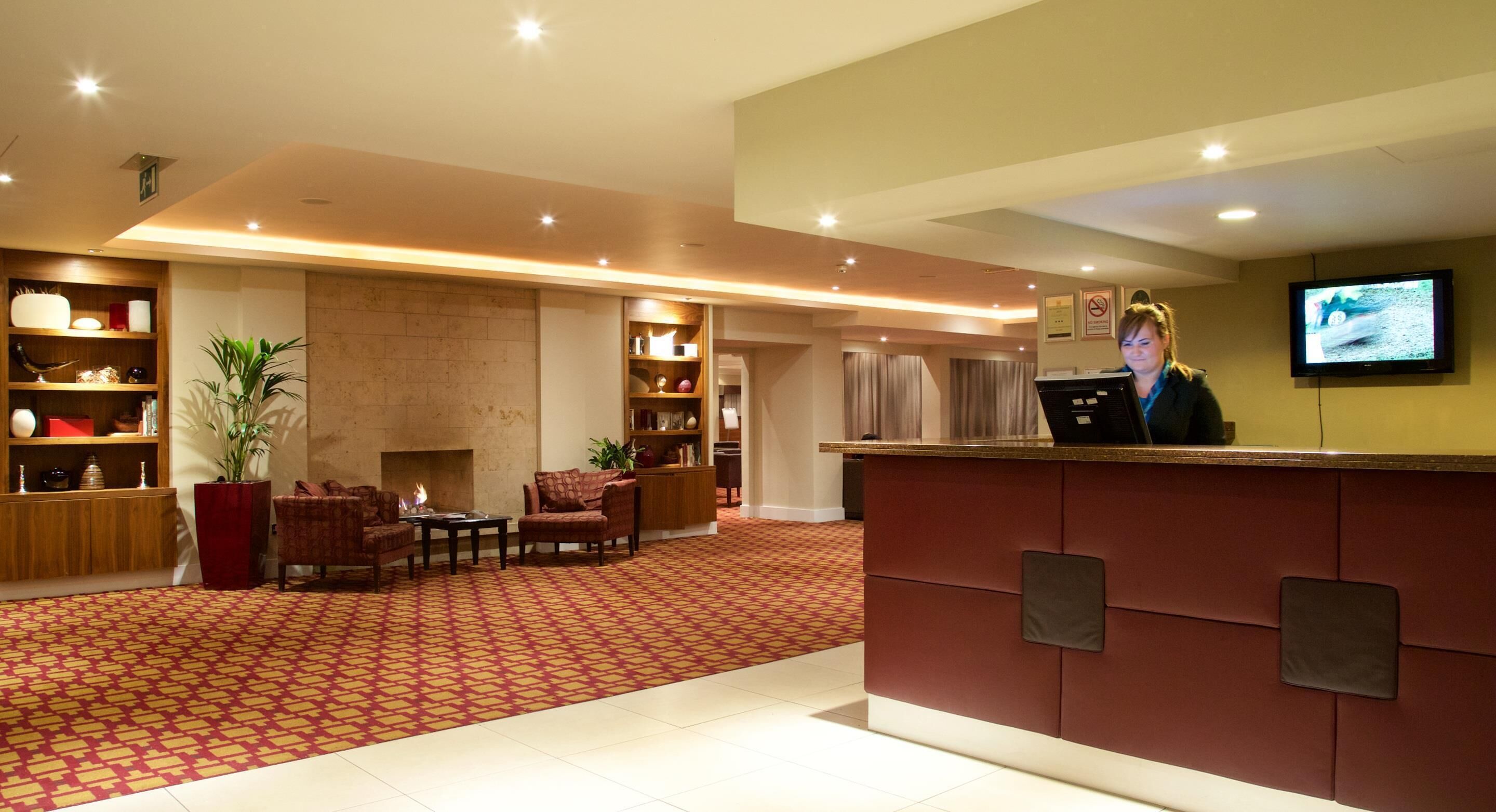 A hotel reception area with a red carpet, wooden furniture, and a television screen.