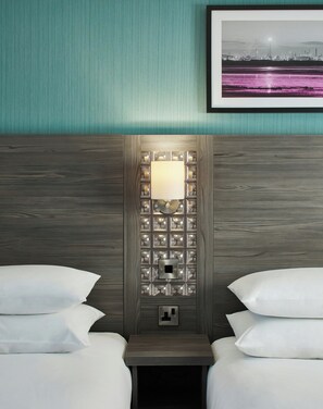 Una habitación de hotel con una cama, una mesita de noche, una lámpara de pared y un cuadro en la pared.