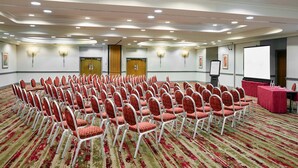 A conference room with rows of red chairs, a projection screen, and a table with a red tablecloth.