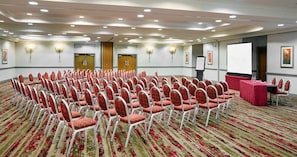 A conference room with rows of red chairs, a projection screen, and a table with a red tablecloth.