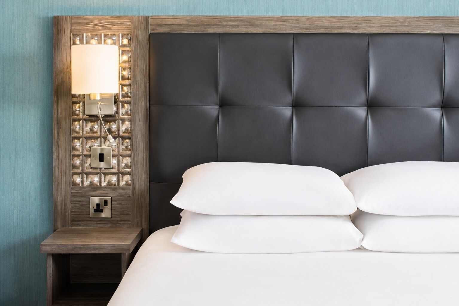 A neatly made bed with white linens and a dark headboard.
