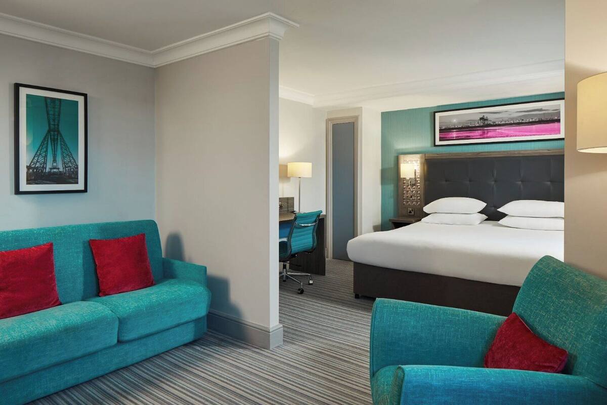 Una habitación de hotel con una cama, un sofá color turquesa y un escritorio.