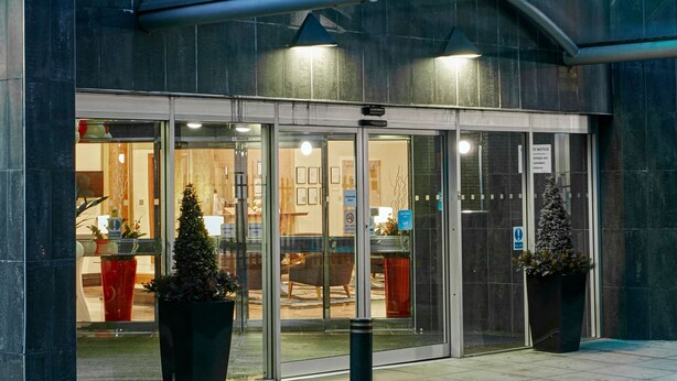 A hotel entrance with a glass door, potted plants, and a sign indicating a smoking area. - Leonardo Hotel Middlesbrough (Middlesbrough)
