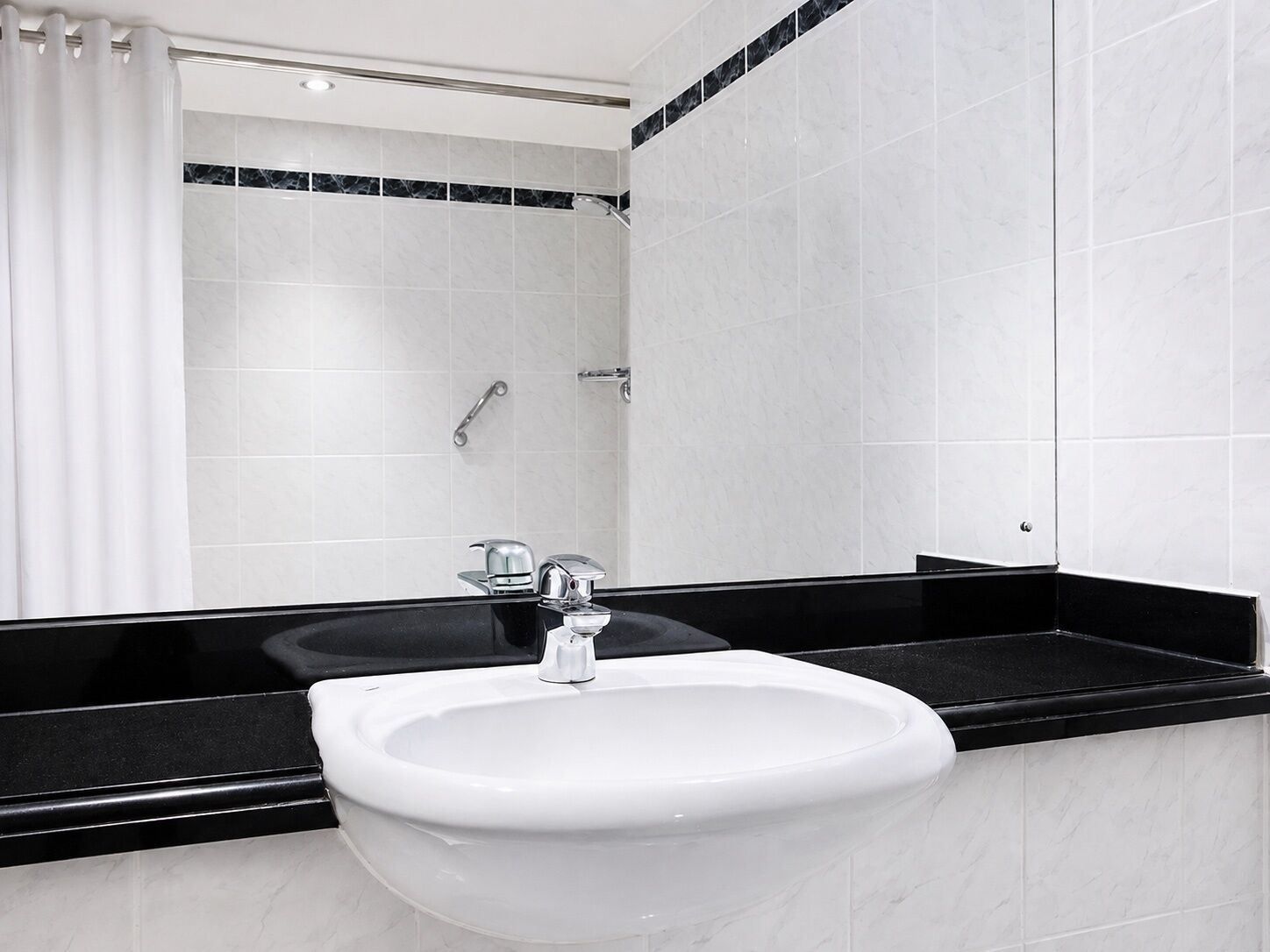 A bathroom with a white sink, black countertop, and a shower area with white tiles and a black-tiled shower enclosure.