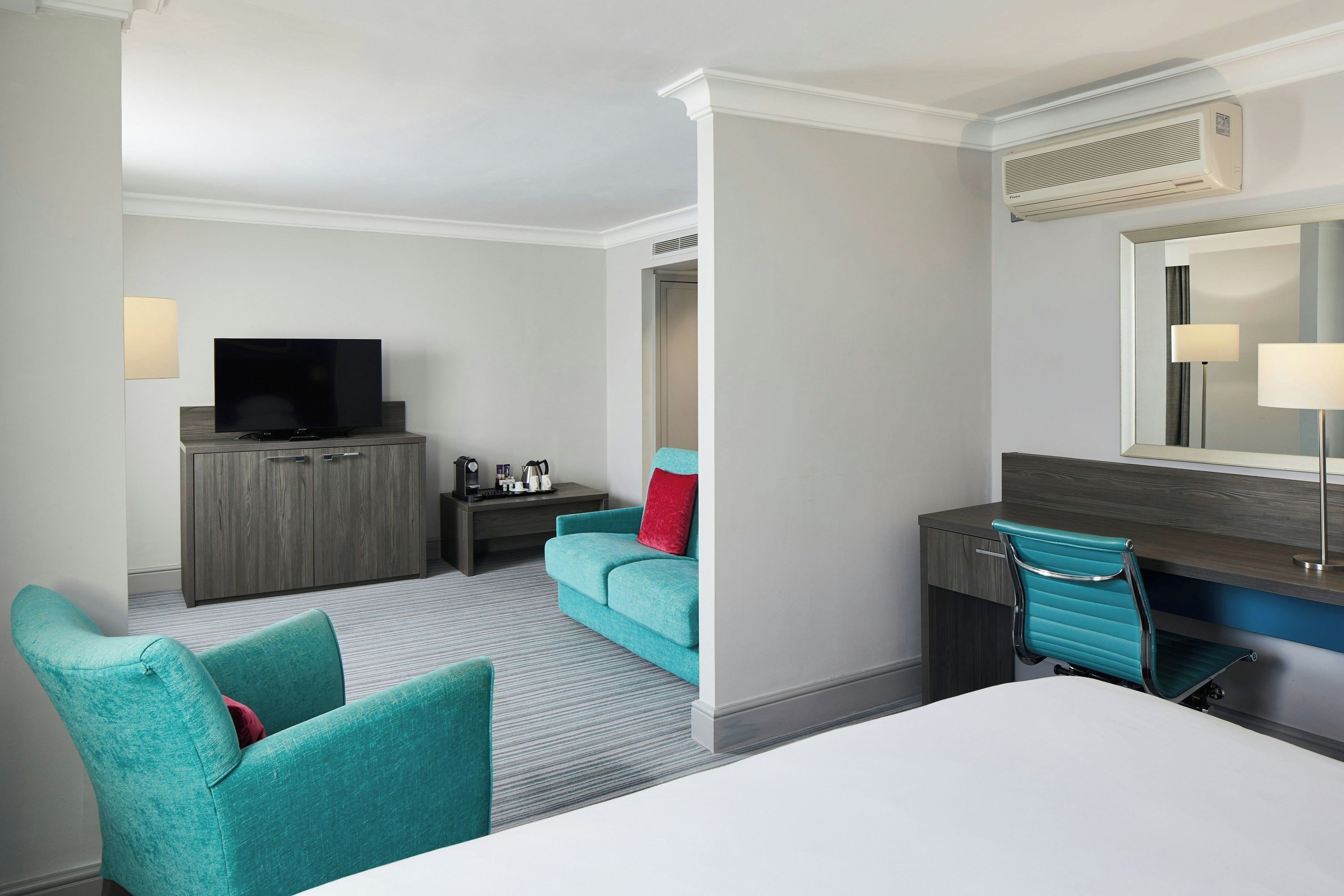 A hotel room with a bed, a desk, a television, a wardrobe, and a seating area with chairs.