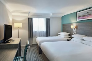 A hotel room with two beds, a flat-screen TV, a desk with a lamp, and a window with curtains. - Leonardo Hotel Middlesbrough (Middlesbrough)