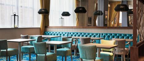 A hotel lobby with a blue and yellow patterned carpet, teal and brown seating, and black pendant lighting.