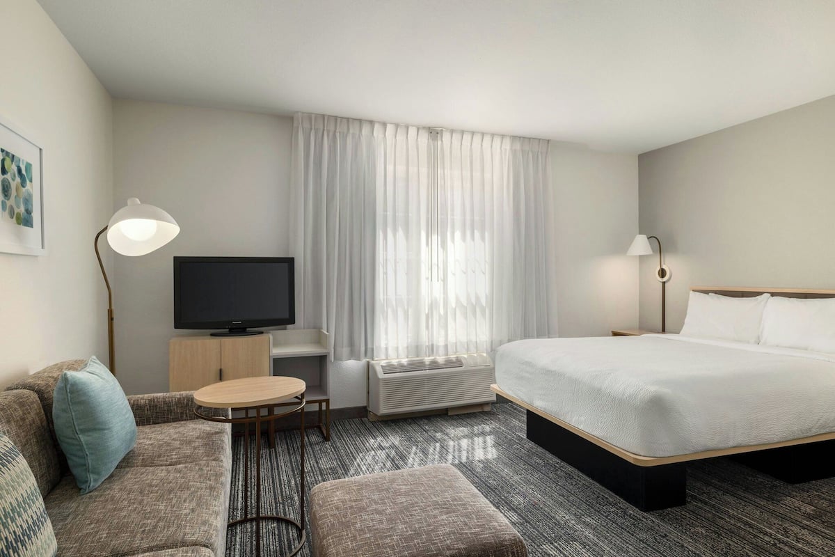 A hotel room with a bed, a sofa, a TV, a desk, and a window with curtains.