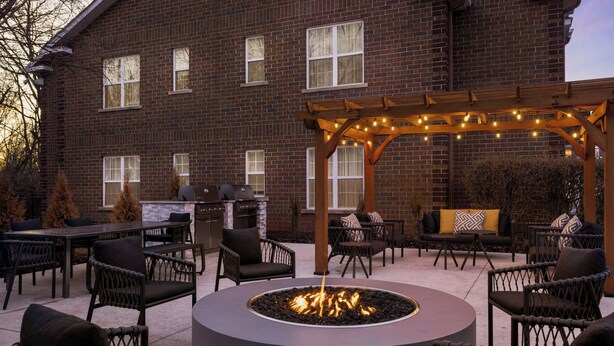 An outdoor patio area with a fire pit, seating, and a pergola with string lights. - TownePlace Suites by Marriott Detroit Dearborn (Dearborn)