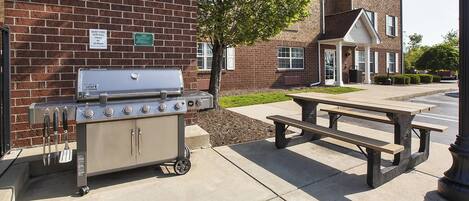 Una parrilla de barbacoa y una mesa de picnic frente a un edificio de ladrillo.