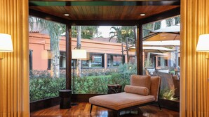 A room with a wooden floor, a cushioned bench, and a view of a building and greenery outside. - Sanma Hotel  (Foz do Iguaçu)