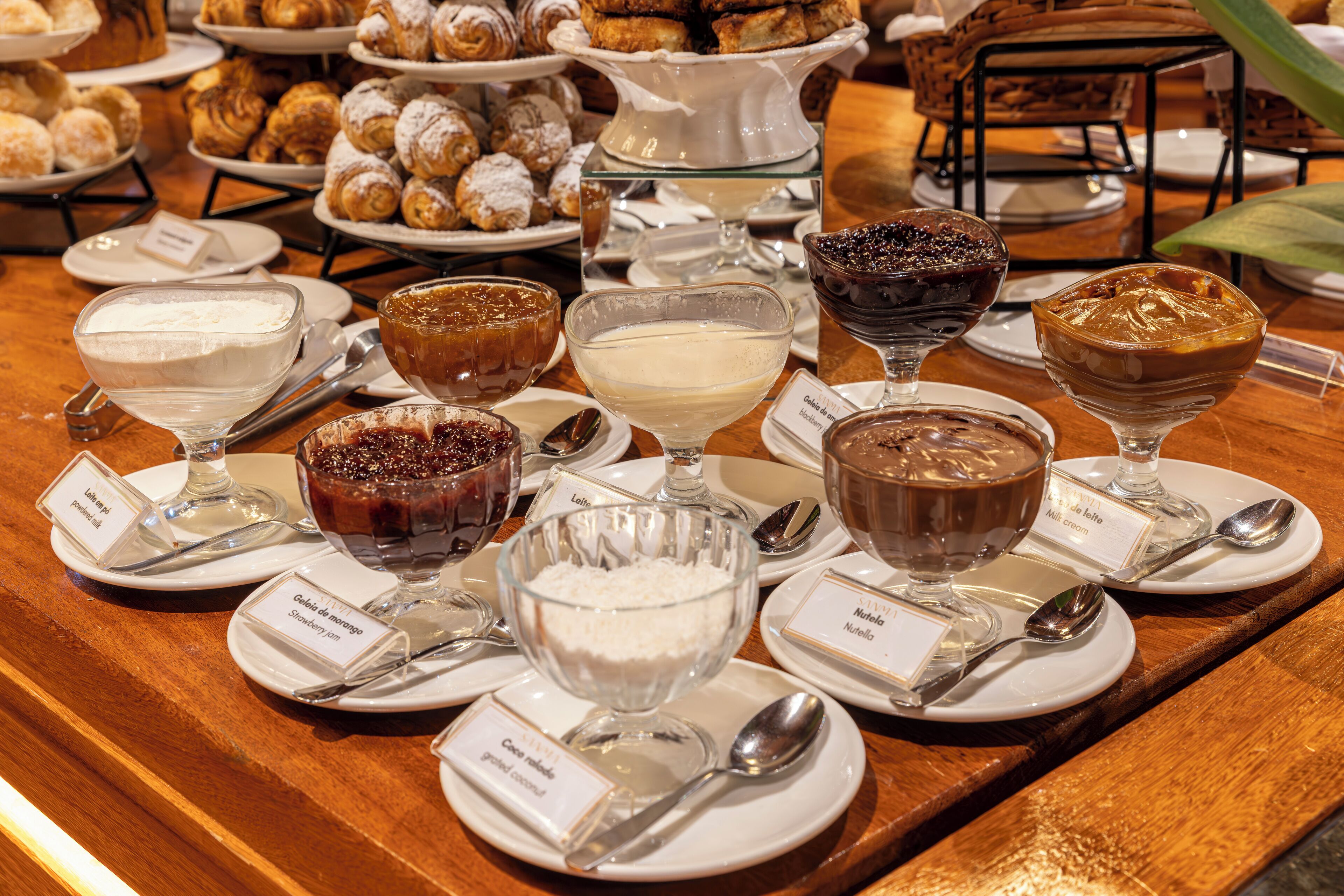 A variety of desserts on a buffet table, including different types of cakes, puddings, and custards, each labeled with their names.