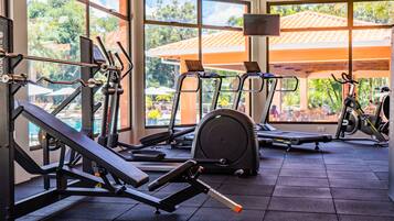 Un gimnasio con diverso equipo de ejercicio, ventanas amplias y vistas al exterior.