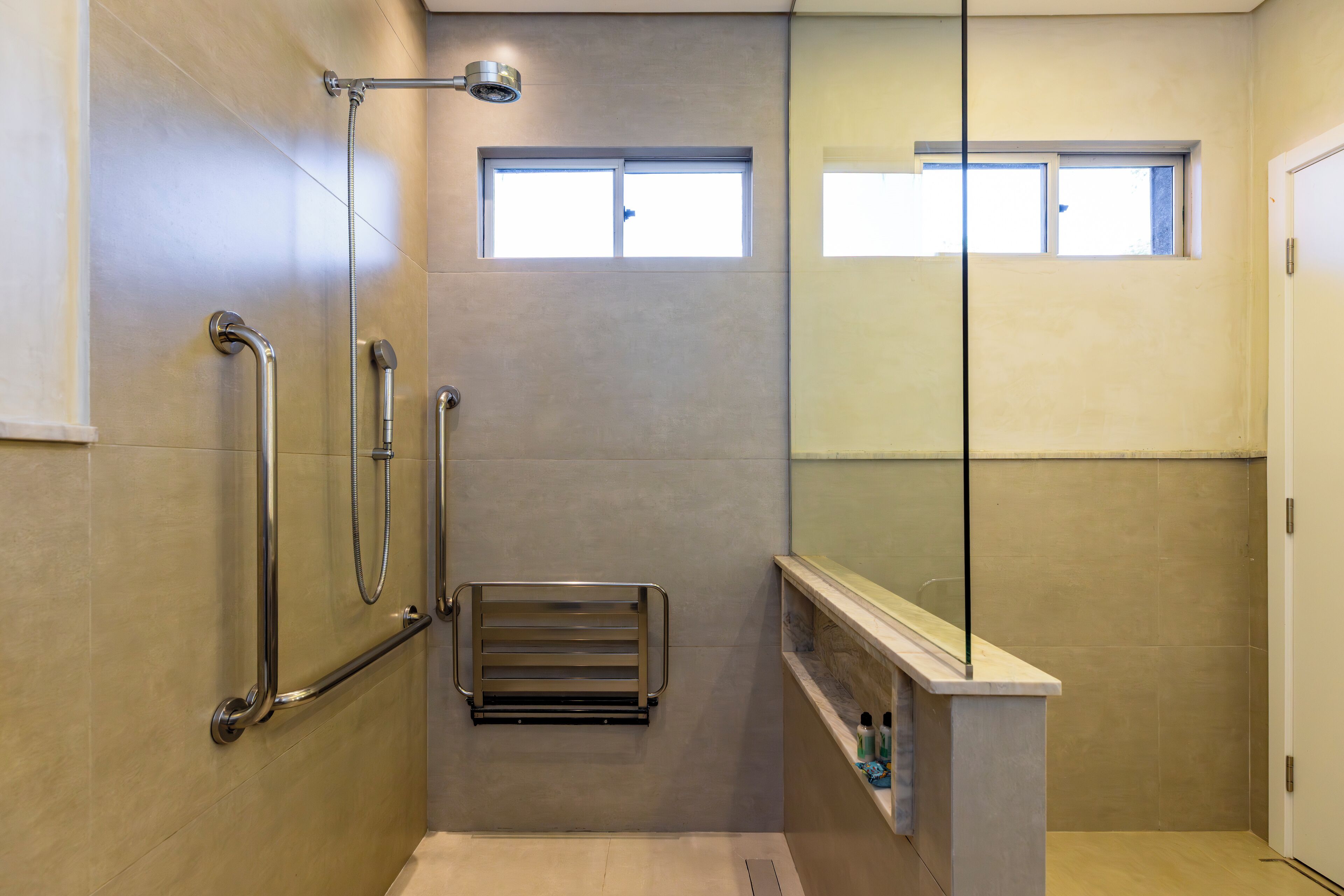 Un baño moderno con cabina de ducha de vidrio, barra de apoyo, toallero y un ventanal.
