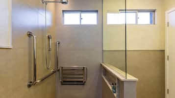 Un baño moderno con cabina de ducha de vidrio, barra de apoyo, toallero y un ventanal.