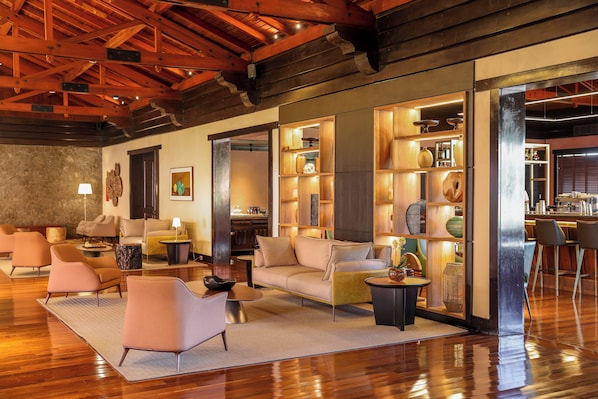 Amplia sala de estar con techo de madera, un conjunto de sofás y una zona de bar con estantes llenos de objetos decorativos.