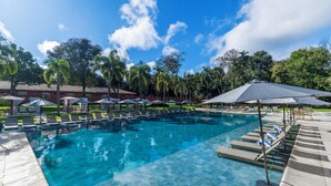 A swimming pool with lounge chairs and umbrellas, surrounded by trees and buildings. - Sanma Hotel  (Foz do Iguaçu)