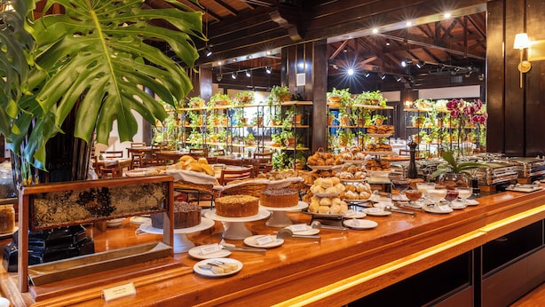 A buffet with various food items and a large plant. - Sanma Hotel  (Foz do Iguaçu)