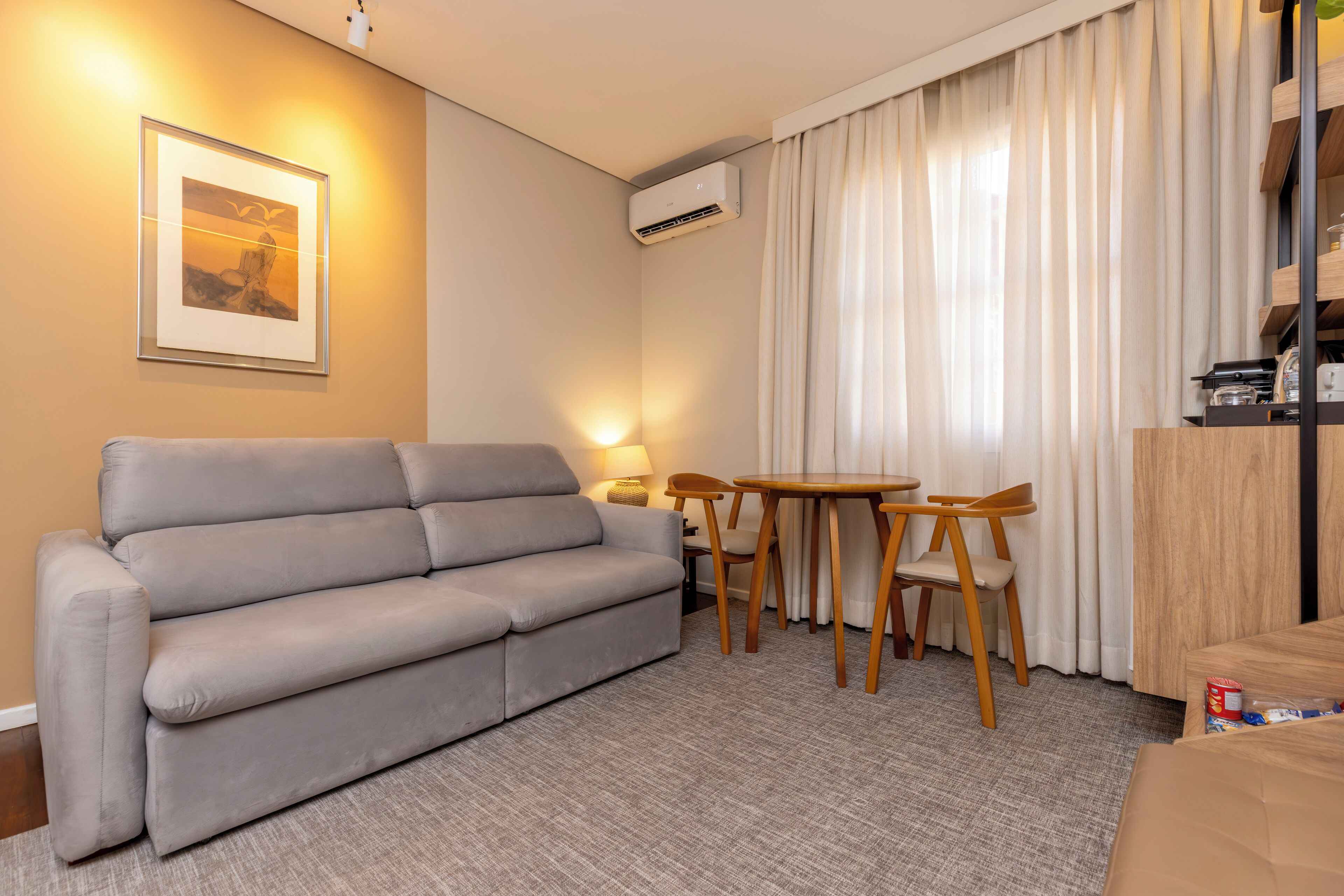 Un salon avec un canapé gris, une petite table en bois avec des chaises, une lampe et un appareil de climatisation.