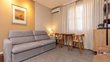 Un salon avec un canapé gris, une petite table en bois avec des chaises, une lampe et un appareil de climatisation.