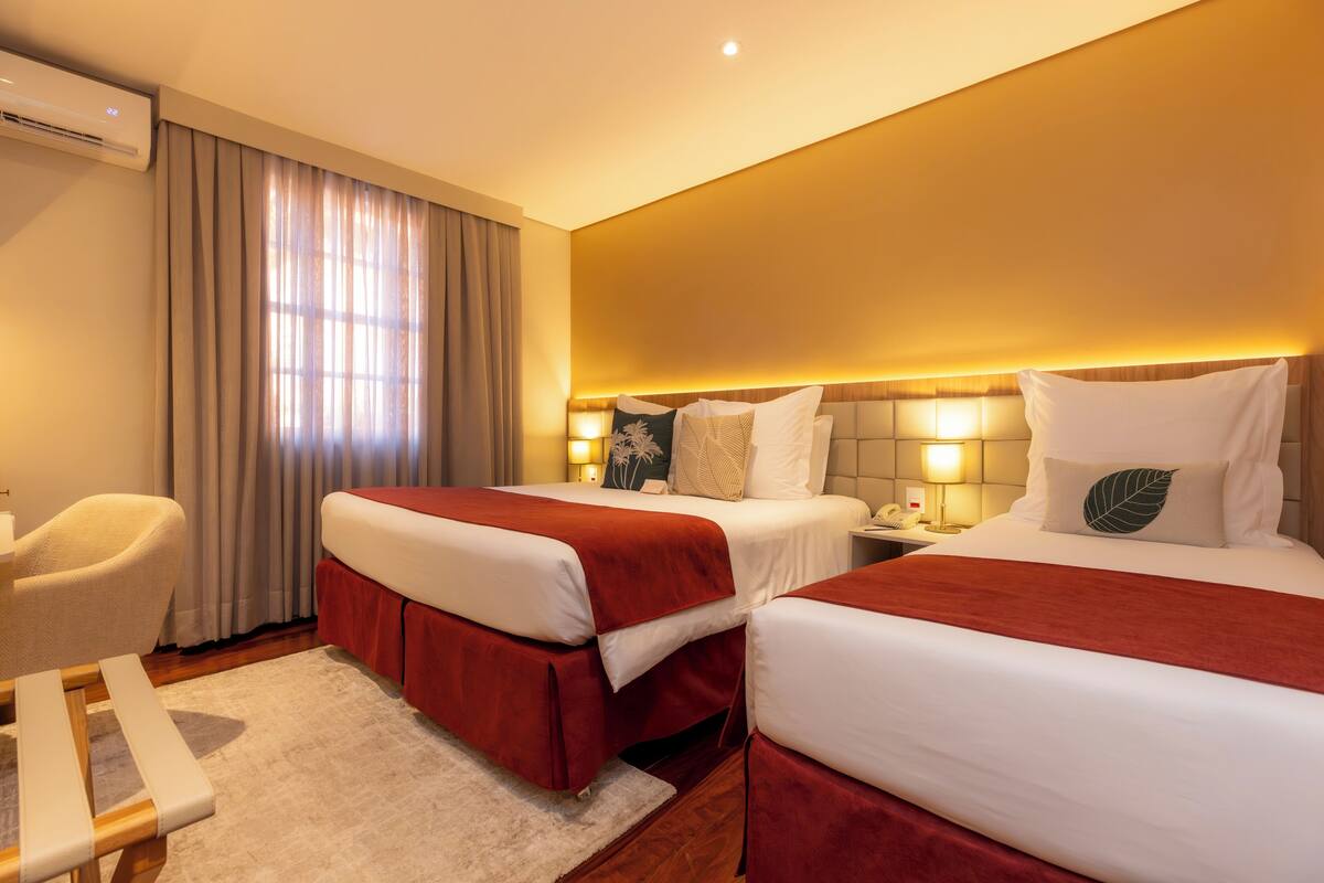 Quarto de hotel com duas camas, uma escrivaninha e uma cadeira.