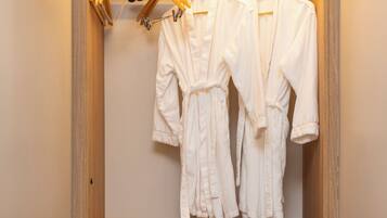 A wooden walk-in closet with two white robes hanging on a rack, a black microwave, and a small drawer unit.