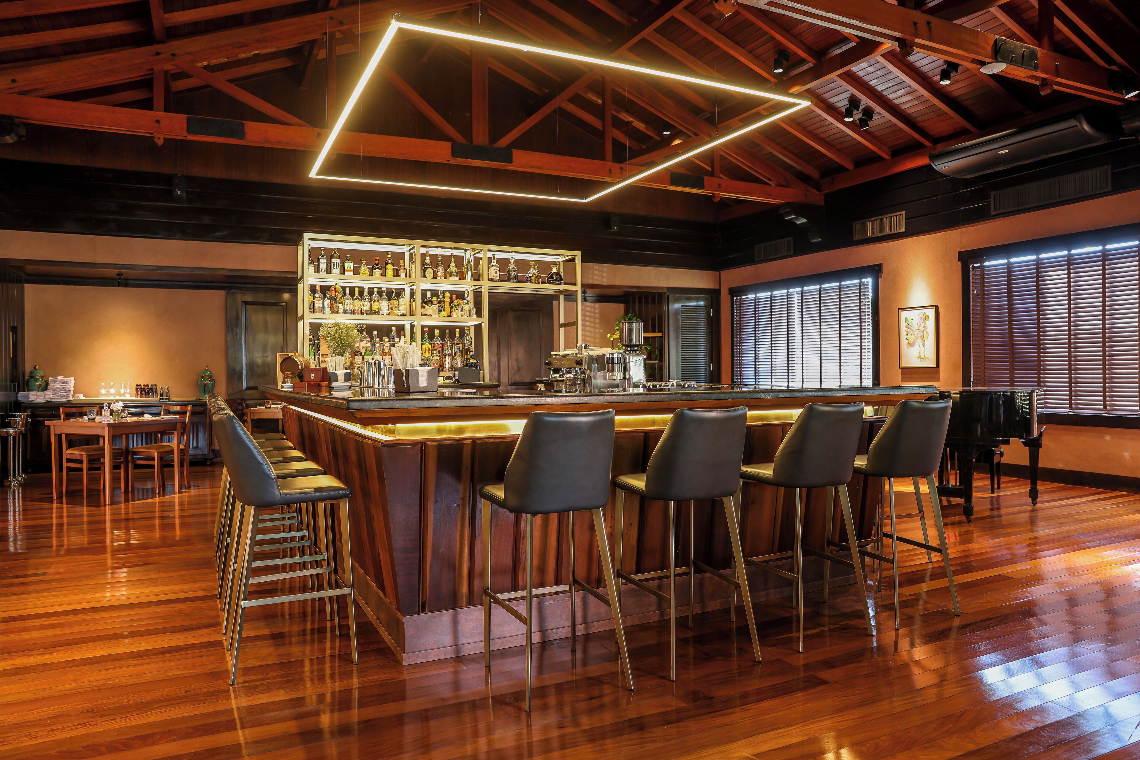 A bar area with a wooden bar counter, bar stools, and a shelf with bottles.