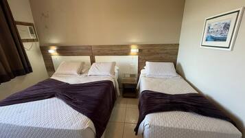 A hotel room with two beds, a nightstand, a wall-mounted air conditioning unit, and a framed picture.