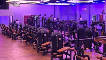 Uma academia com diversos equipamentos de exercícios, piso de madeira e iluminação roxa.