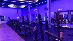 A gym with various exercise equipment, including weight machines and free weights, under blue lighting. - Brisamar Suite Hotel (Florianópolis)