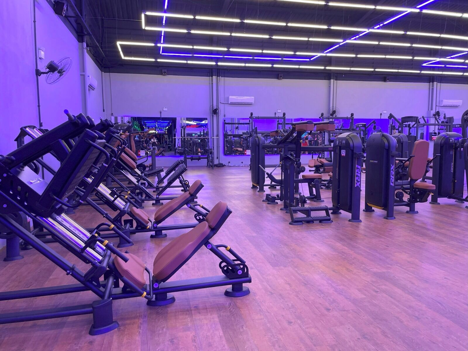 A gym with exercise equipment, wooden flooring, and purple lighting.