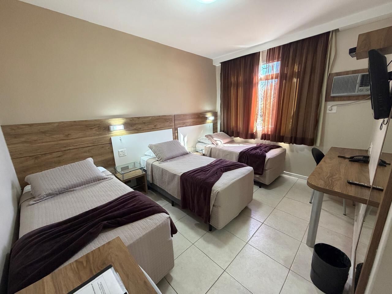 Habitación de hotel con dos camas, un escritorio, una silla, un cesto de basura y una ventana con cortinas.