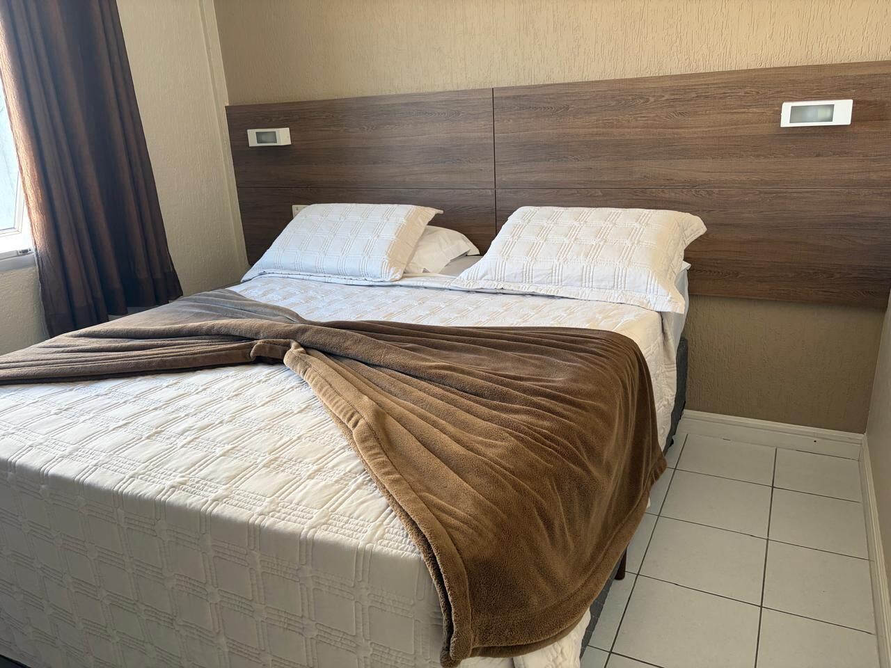 Une chambre d’hôtel avec un lit, une tête de lit et une fenêtre avec des rideaux.
