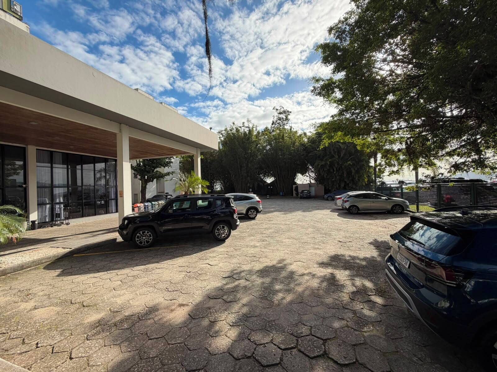 Un estacionamiento con entrada a un edificio, coches aparcados y cielo despejado.