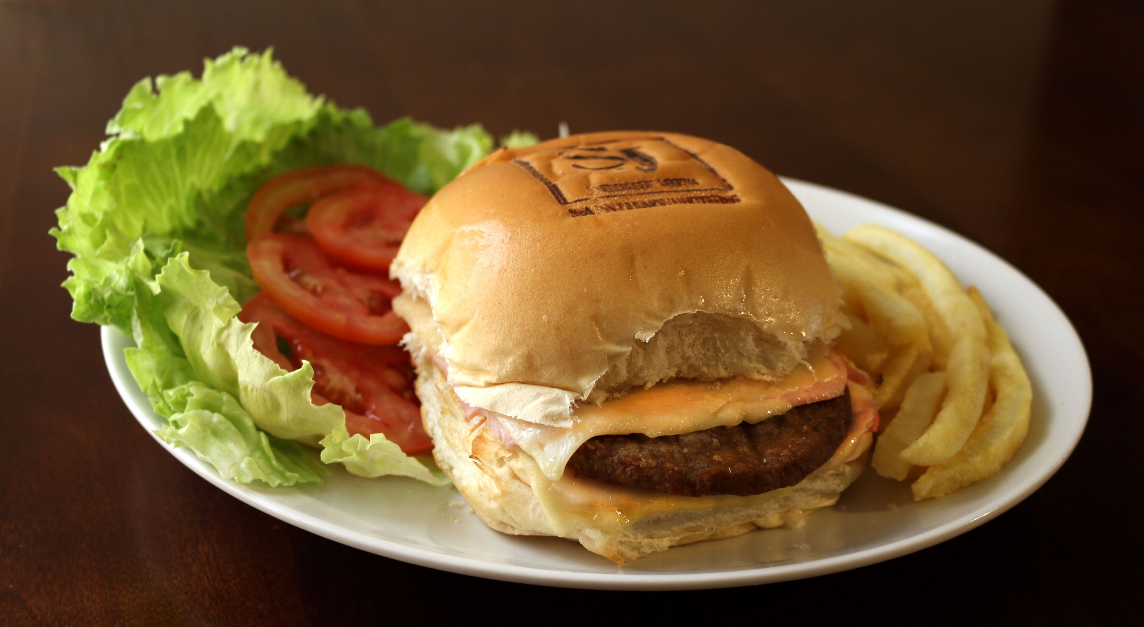 A hamburger with lettuce, tomato, and fries on a white plate.
