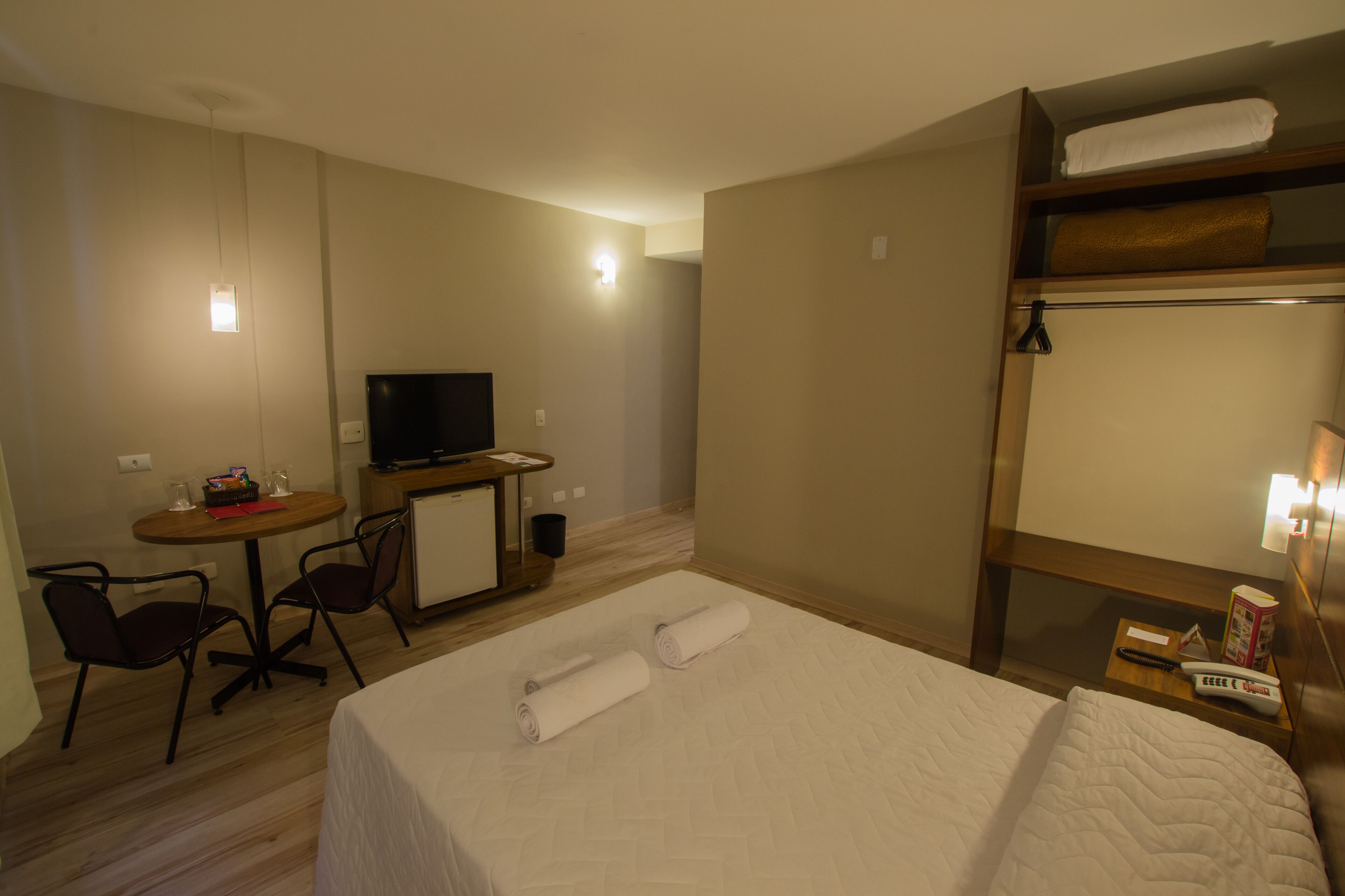 A hotel room with a bed, a desk with a television, a chair, and a bunk bed.