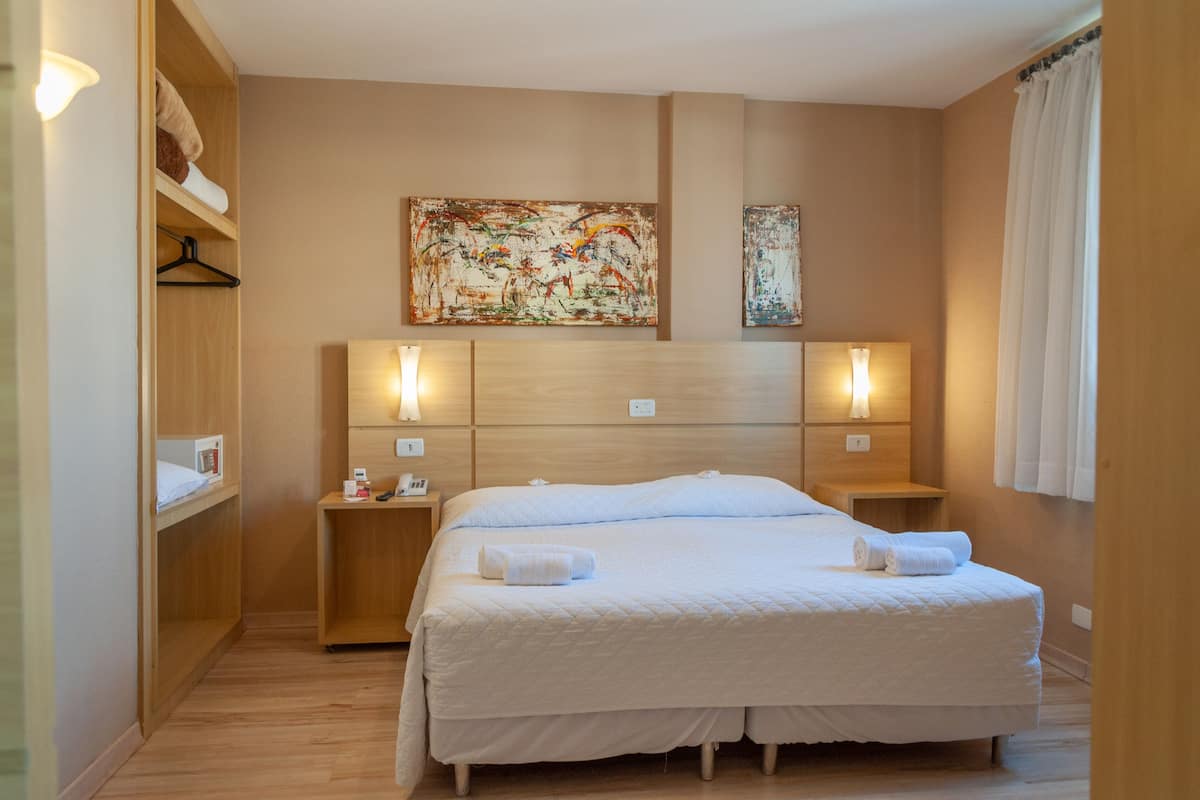 Een hotelkamer met een groot bed, een houten hoofdeinde, bedlampjes en een schilderij aan de muur.