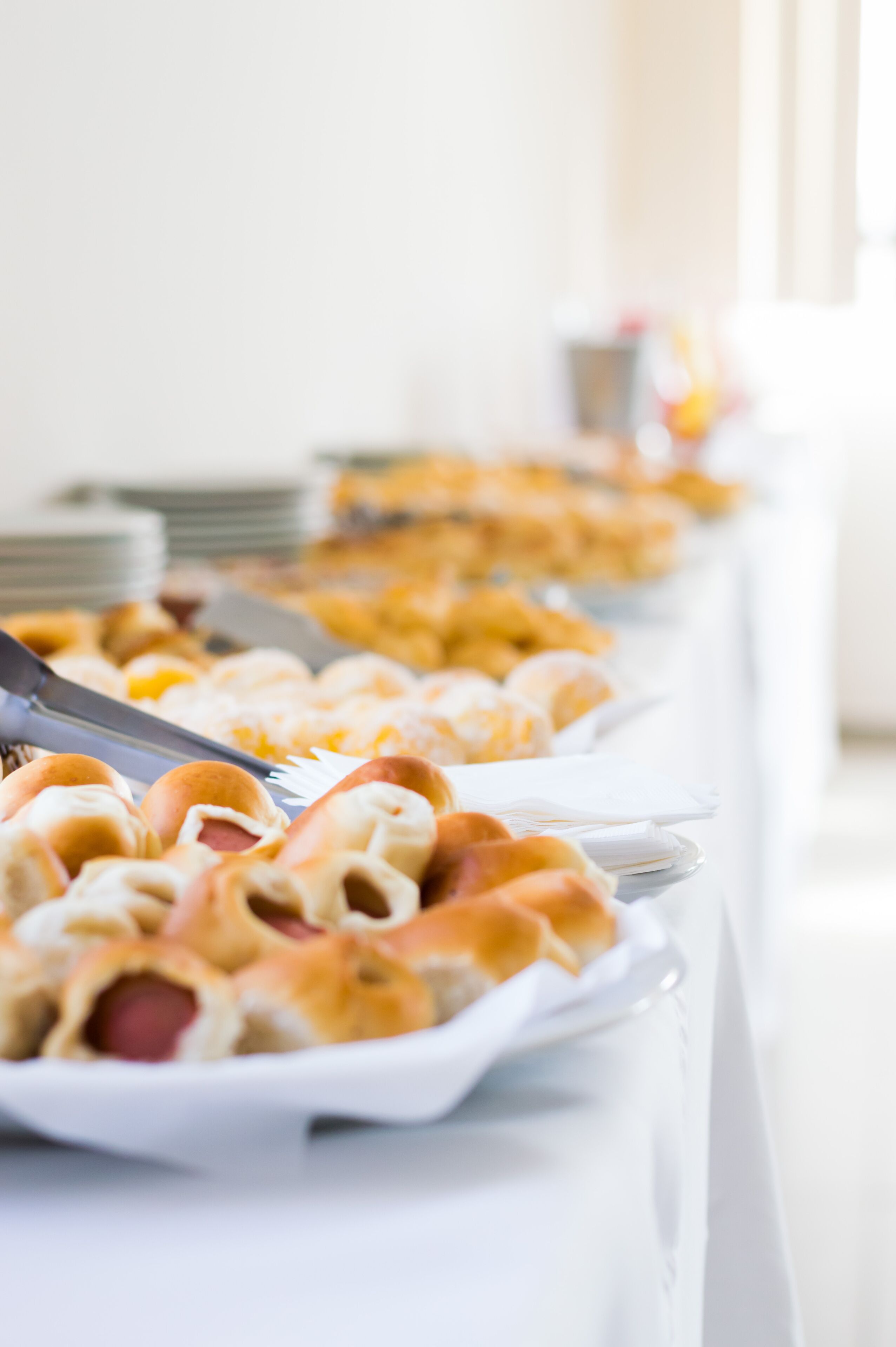 Una mesa de buffet con diversos alimentos, incluyendo panes y pasteles, dispuestos en platos blancos.