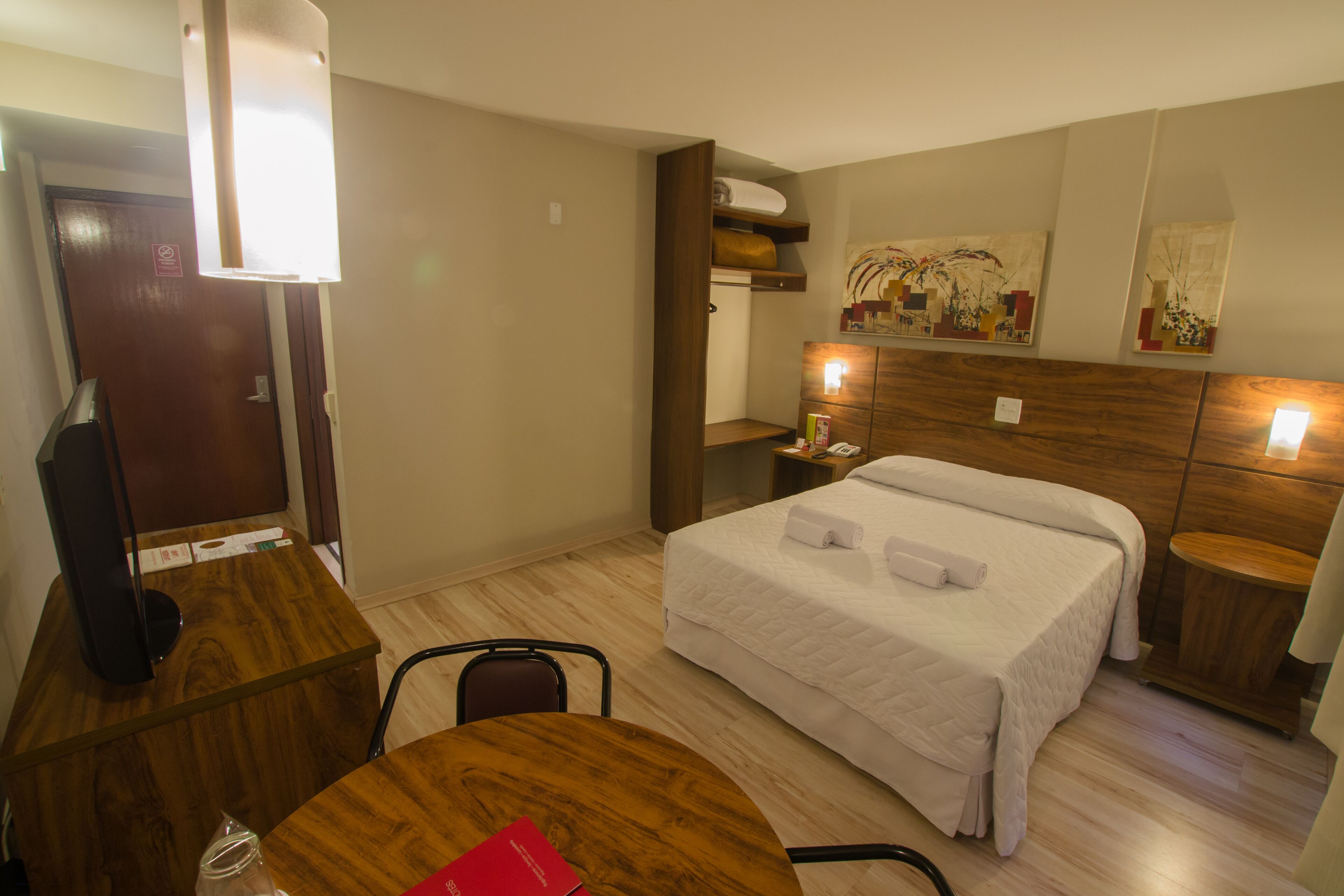 Habitación de hotel con cama, escritorio, silla, mesita de noche y un cuadro en la pared.
