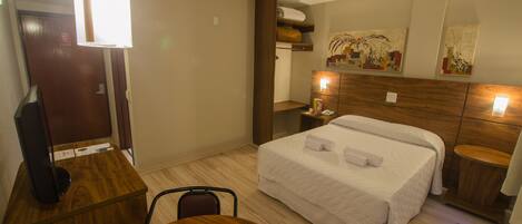 Habitación de hotel con cama, escritorio, silla, mesita de noche y un cuadro en la pared.