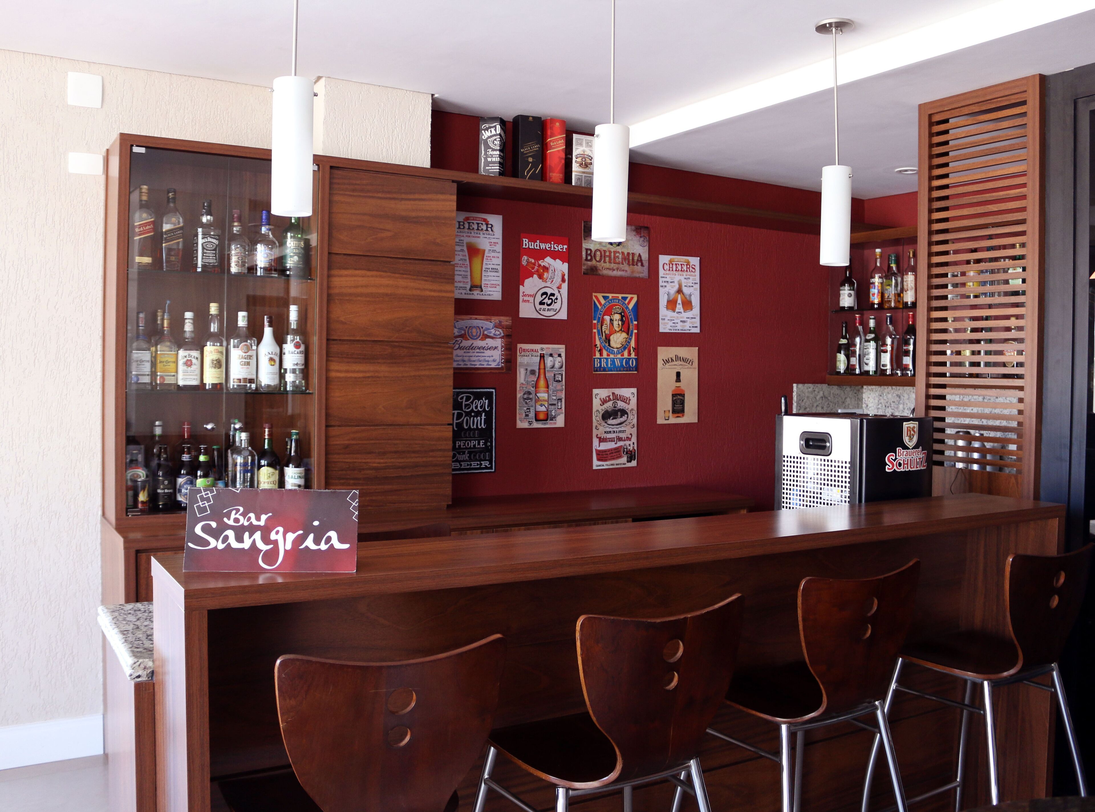 Un área de bar con mostrador de madera, taburetes y un refrigerador. Hay carteles en la pared y un letrero que dice "Bar Sansaria".