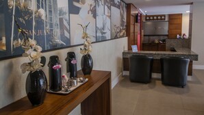 Et receptionområde med et træskrivebord, sorte vaser med orkideer, en kaffemaskine og et stort plakatbillede af San Juan Hotels.